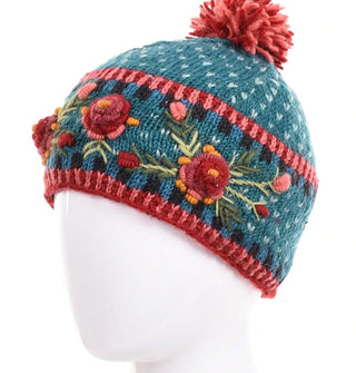 Teal wool beanie with textural purple, gold, and green floral embroidery, geometric border designs, and a two-tone pink and red pom pom on top