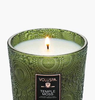 Single lit wick of a Temple Moss Voluspa candle in a green embossed glass vessel
