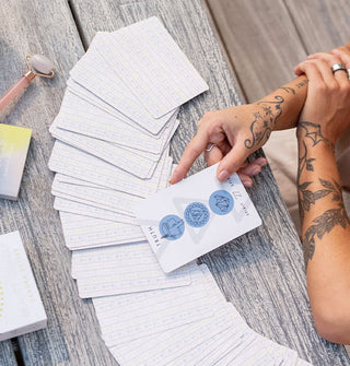 Model draws a card from a fanned-out spread of The Beauty Oracle on a wooden tabletop
