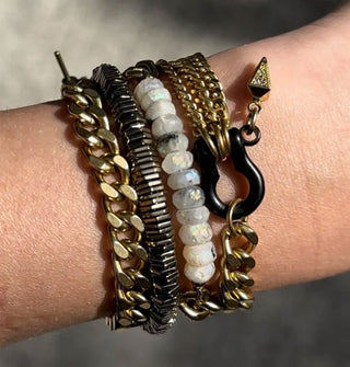 Model's wrist wears a set of four chain and stone bracelets with clasp and charm details