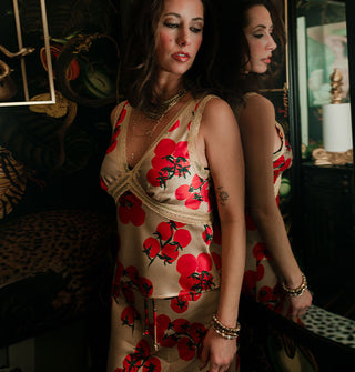 Model standing with back to a mirror in which she is reflected wears a satin tomato print lace-trimmed camisole top with matching skirt