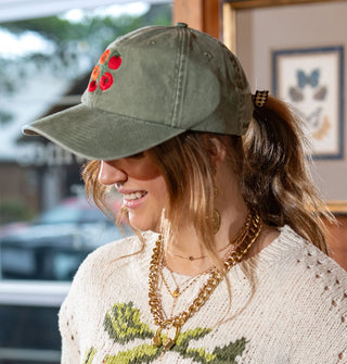 Smiling model wears a sage green baseball cap with vibrant red tomato vine embroidery