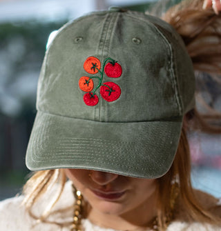 Closeup of the red and green tomato vine embroidery on the front of a sage green baseball cap