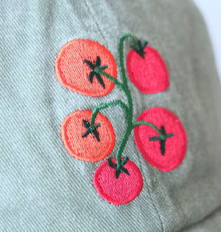 Closeup of the red and green tomato vine embroidery on the front of a sage green baseball cap