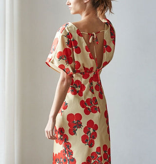 Model facing away from the camera wears a dress with bell sleeves, empire waist, tie back, and print of tomatoes on the vine