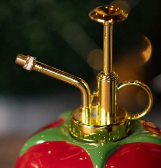 Plant mister with gold top hardware and a a ceramic base designed to resemble a red tomato with green leaves