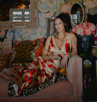 Model reclining on a pink velvet couch with leopard print accents against a floral backdrop hung with mirrors wears a satin tomato print skirt and matching camisole with lace trim