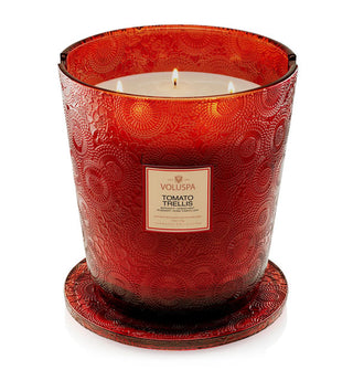 Lit 5-wick Tomato Trellis Voluspa candle in a red embossed glass vessel with matching lid removed and placed underneath as a coaster