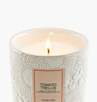 Single lit wick of a Tomato Trellis Voluspa candle in a white embossed ceramic vessel