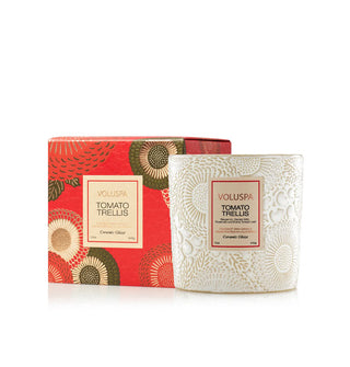 White embossed Tomato Trellis Voluspa candle vessel is situated next to its red, green, and gold floral patterned gift box