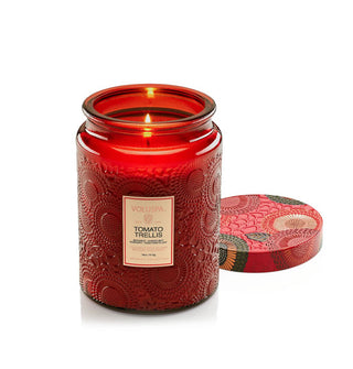 Lit Tomato Trellis Voluspa candle in a red embossed glass jar with colorful floral print embossed tin lid removed and set to the side