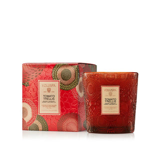 Embossed red glass Tomato Trellis Voluspa candle vessel situated next to its corresponding gift box with metallic floral embossed patterning