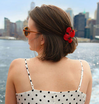 Model standing against a backdrop of city skyline wears a white dress with black polka dots and a red cherry tomato claw clip in a partial updo