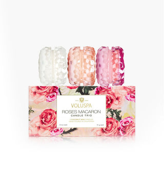 Three faceted glass macaron-style candle jars are placed on end atop a decorative rose-patterned Roses Macaron Candle Trio gift box by Voluspa