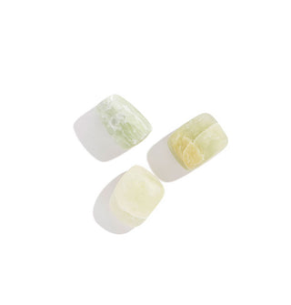 Grouping of three greenish-yellow tumbled matte xiuyan jade stones, all with slightly different shapes, sizes, and patterning