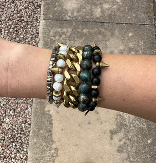 Model wears a mix of brass and round gemstone bracelets photographed above a sidewalk