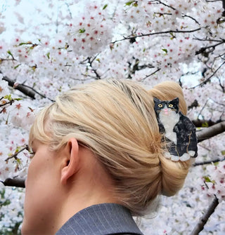 Model standing in front of white cherry blossoms wears a tuxedo cat claw clip in a twist updo hairstyle