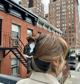Model standing in front of a cityscape wears a tuxedo cat claw clip in a loose updo hairstyle