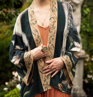 Model wears a dark cropped kimono-style open-front top with floral and swan designs complemented by a printed beige border and cuffs