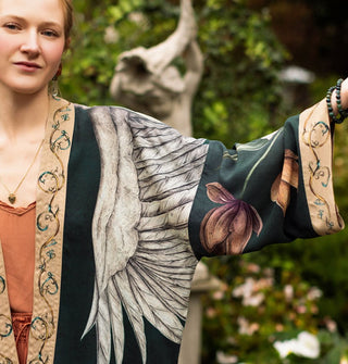 Model wearing a dark green kimono-style garment with swan and floral designs complemented by a printed border and cuff extends one arm to show sleeve details