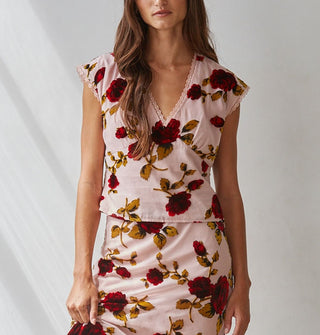 Model wears a cap-sleeved blouse with lace trim, empire waist, and bold red rose print paired with matching skirt