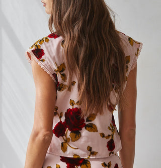 Model facing away from the camera wears a cap-sleeved blouse with lace trim and bold red rose print