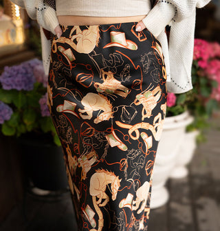 Model wearing a black satin skirt with tan and red cowboy hats, saddles, and horses print