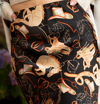 Model wearing a black satin skirt with tan and red cowboy hats, saddles, and horses print