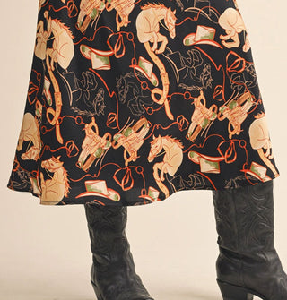 Model wears a black satin midi skirt with ta and red horses, cowboy hats, and saddles print with black cowboy boots 