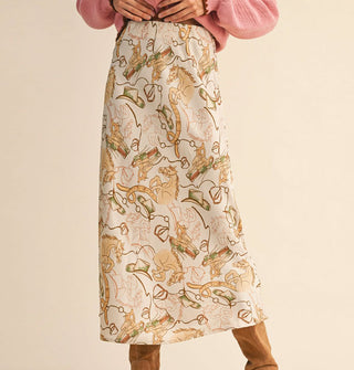 Model wearing a long cream-colored satin skirt with tan, green, and orange cowboy hats, saddles, and horses print