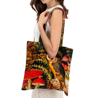 Model holds a tote bag over shoulder that features a scene of a barn own perched on a tree stump amid mushrooms and ferns