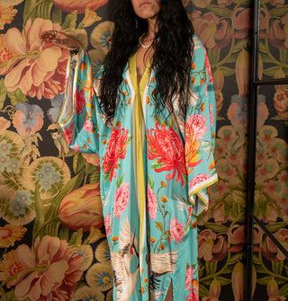 Model wears a long, flowing blue robe with bold floral print and contrast stripe edging