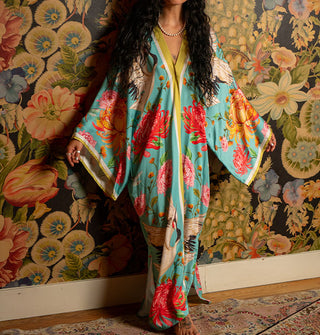 Model wears a long, flowing blue robe with bold floral print and contrast stripe edging