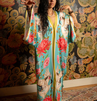 Model wears a long, flowing blue robe with bold floral print and contrast stripe edging