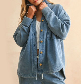 Model pulls up the collar of a soft-washed blue shirt-jacket with gold buttons that she wears paired with matching drawstring pants
