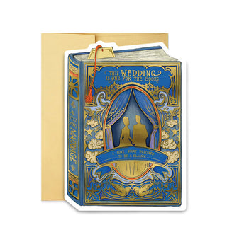 Blue greeting card in front of a gold envelope features a gold silhouette of a couple inside an ornate gold-accented, curtained cameo frame over which a banner reads, "A love story destined to be a classic," and the words, "This wedding is one for the books" at the top; on the spine is the message, "A very merry marriage" in gold