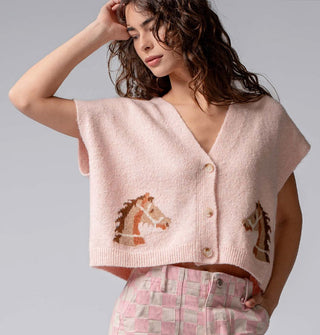 Model wears a light pink short-sleeved V-neck cropped cardigan with three buttons and two mirrored bridled brown horse designs near the bottom hem on either side of the button placket