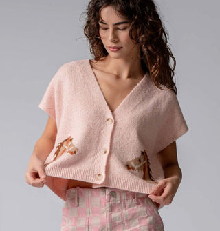 Model wears a light pink short-sleeved V-neck cropped cardigan with three buttons and two mirrored bridled brown horse designs near the bottom hem on either side of the button placket