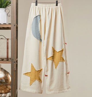 White wide-legged pants with blue-gray moon and yellow stars appliqués on the back, all with rough edges
