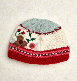 Knit beanie with pink, white, and red striped border, white middle with floral embroidery, and a gray tip separated from the white middle by red vine-like stitching
