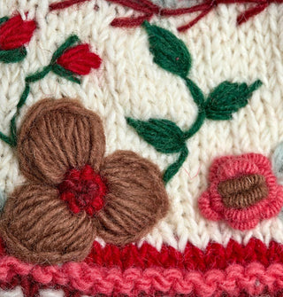 Closeup of knit floral embroidery in pink, red, brown, green, and white