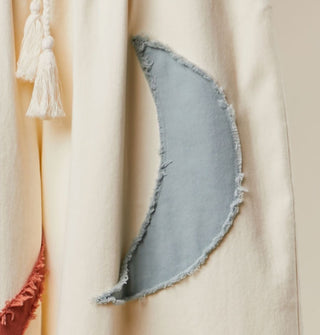 Closeup of a rough-edged blue-gray crescent moon appliqué on white fabric
