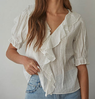 Model wears a ruffly white blouse with pleated details and short balloon sleeves