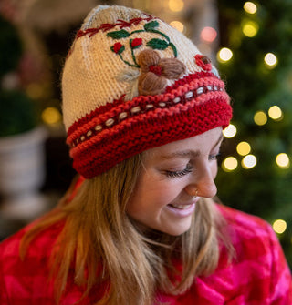 Smiling model wears a knit beanie with pink and red striped border, white middle with floral embroidery, and a gray tip