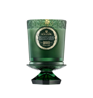 Lit green glass Voluspa candle jar with decorative label is placed atop its pedestal-shaped lid