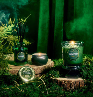 Decorative candles and diffuser staged on natural wood platforms against a mossy, misty backdrop