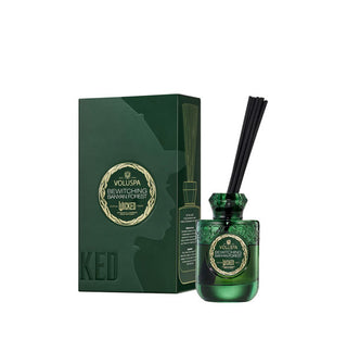 Green glass Voluspa oil diffuser bottle with black reeds inserted sits next to its matching decorative gift box