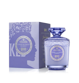 Embossed purple Wicked edition Cherry Blossom Bubble Voluspa candle jar with gem-shaped lid handle next to its matching gift box which features Glinda's silhouette