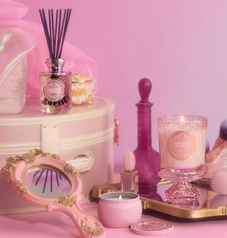 Pink and gold decorative items including candles, a mirror, and bottles on a pink background