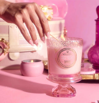 Model's hand lights a Voluspa Perfectly Pink Yuzu Wicked pedestal candle with a wooden match